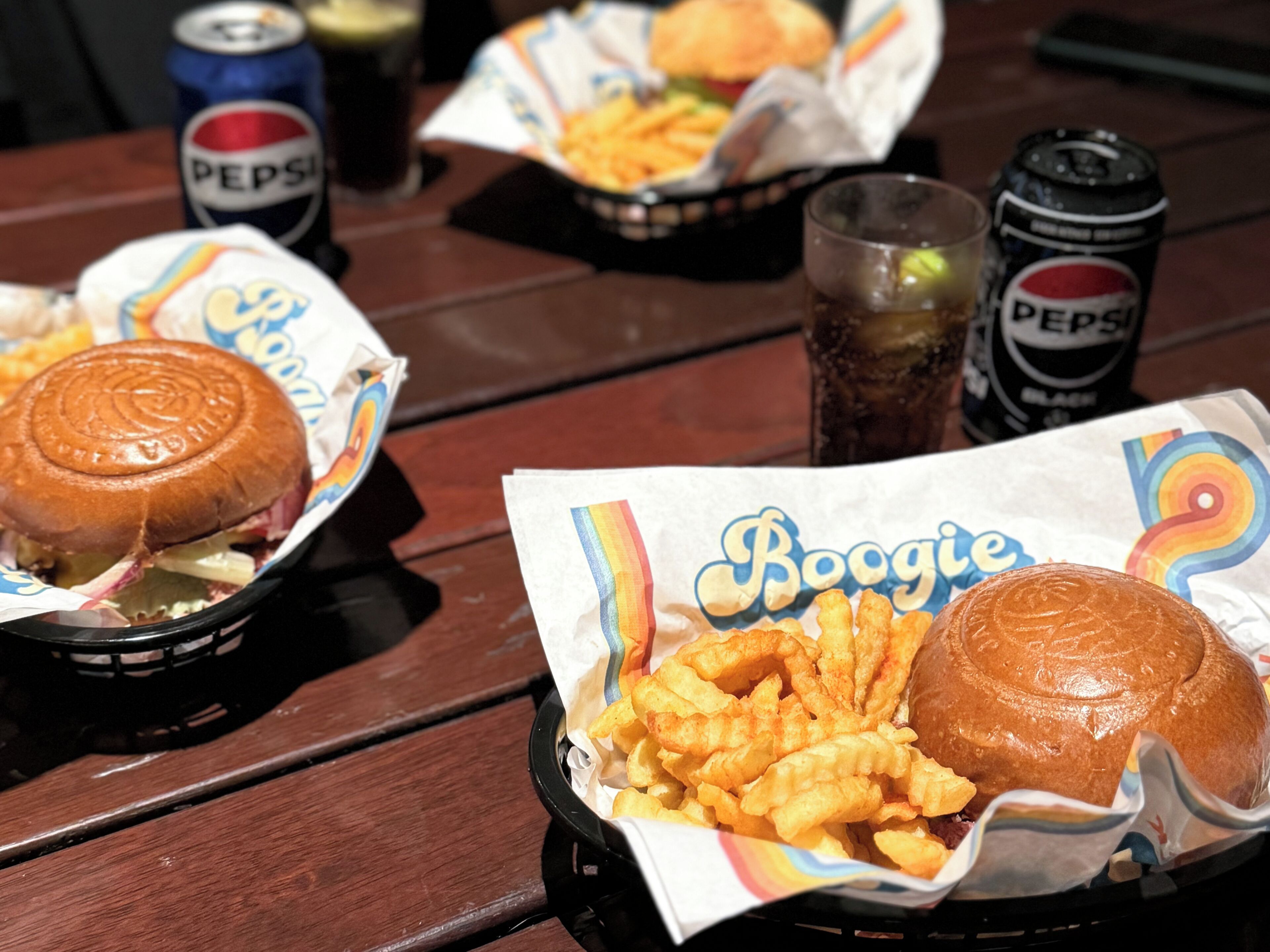 Uma refeição com hambúrguer, batatas fritas e bebidas sobre uma mesa de madeira.