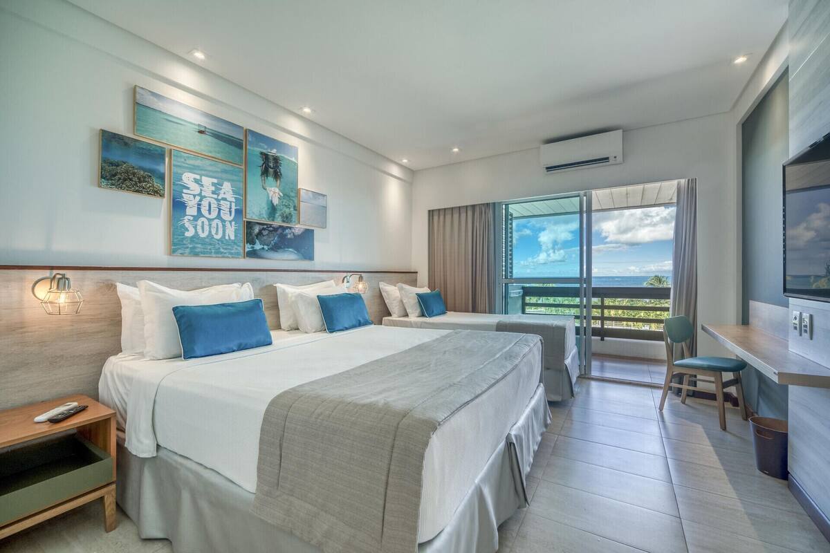 Une chambre d’hôtel avec deux lits, un bureau, une chaise, une télévision et un balcon avec vue.
