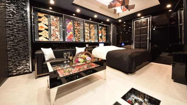 A modern hotel room with a large bed, a seating area with a glass coffee table, and a decorative wall with patterned artwork. - Hotel SARA Kawagoe - Adults Only (Kawagoe)