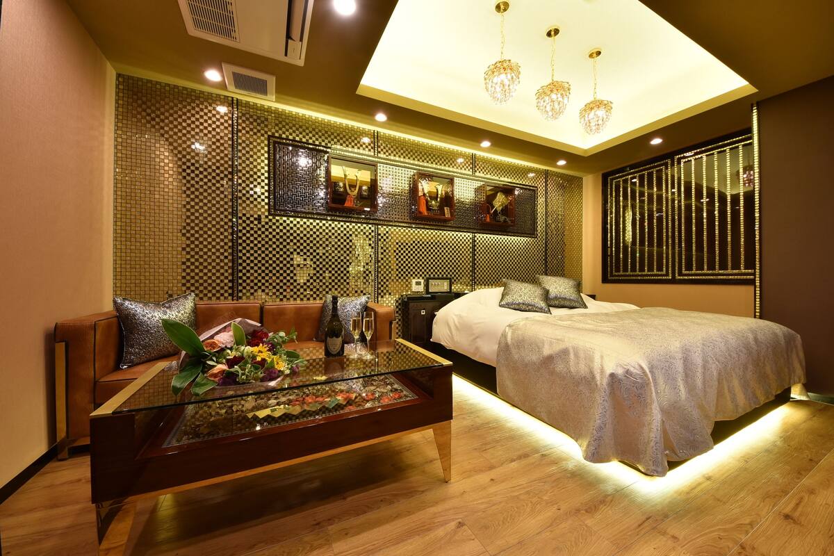 Une chambre d’hôtel moderne avec une table basse en verre, un canapé, un lit et un mur décoratif agrémenté de miroirs et de jeux de lumière.