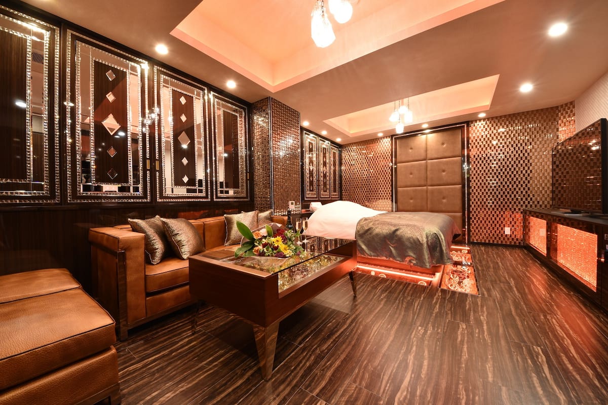 Une chambre d’hôtel moderne avec un grand lit, un canapé, une table basse agrémentée de fleurs et un grand miroir.