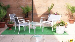 A patio area with two white chairs and a small table, surrounded by potted plants and a green artificial turf. - Mi Casa Affittacamere (Osio Sotto)