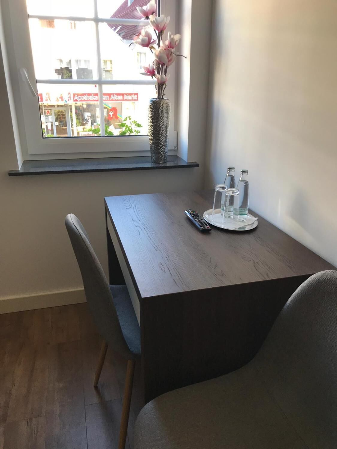 A dining area with a table, chairs, a vase with flowers, and a window with a view of buildings.