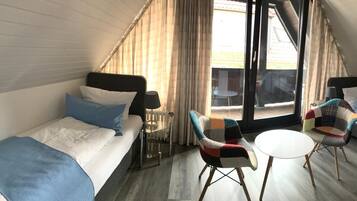 A compact room with a bed, two chairs, a small table, and a large window.