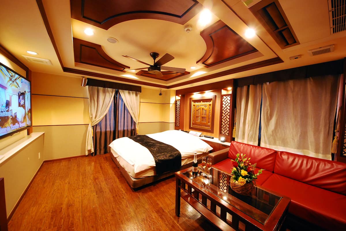 A hotel room with a bed, a red sofa, a wooden coffee table, and a television on the wall.