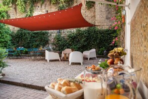 An outdoor seating area with white chairs, a red canopy, and a table with food and drinks. - Borgo Vergini Garden (Naples)
