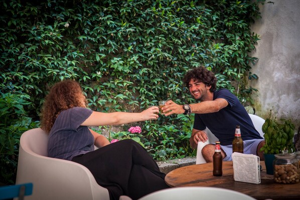 Two people toasting with drinks at a table with a bottle and a jar of nuts. - Borgo Vergini Garden (Naples)