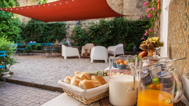 A breakfast setup with bread, milk, and orange juice on a table, with outdoor seating and greenery in the background. - Borgo Vergini Garden (Naples)