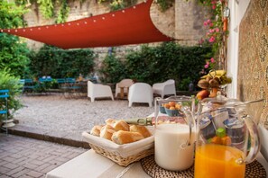 A breakfast setup with bread, milk, and orange juice on a table, with outdoor seating and greenery in the background. - Borgo Vergini Garden (Naples)