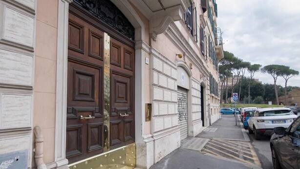 A building with a large, ornate wooden door, a parking area with cars, and a clear sky. - Rome Vatican Inn (Rome)