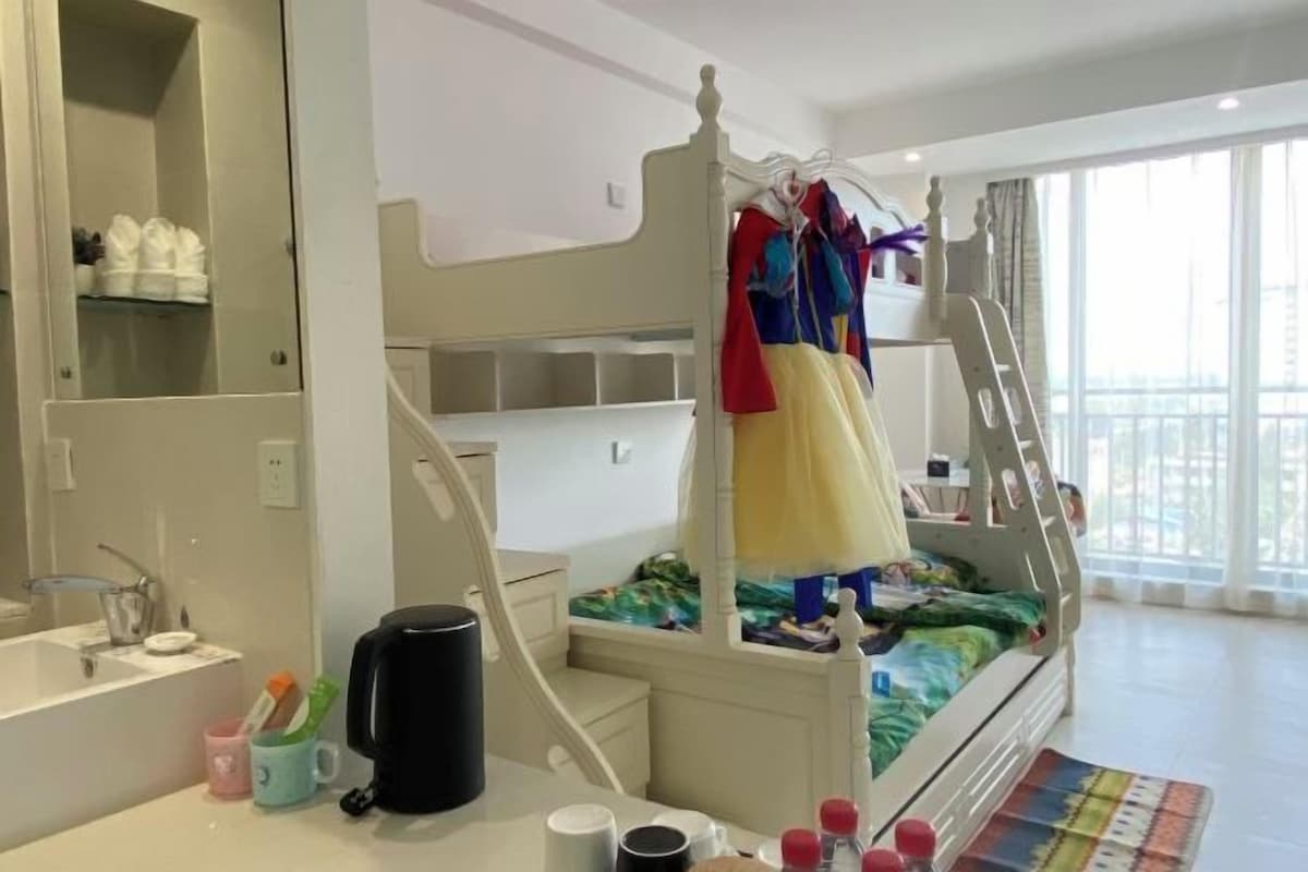 A child's bedroom with a bunk bed, a desk with a chair, a mirror, and a window with a view.