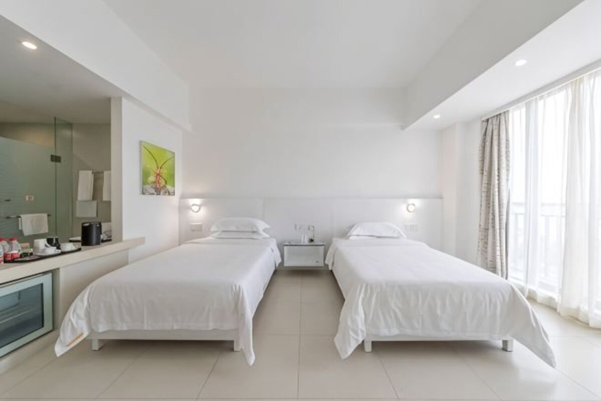 A hotel room with two beds, a desk with a mirror, and a large window.