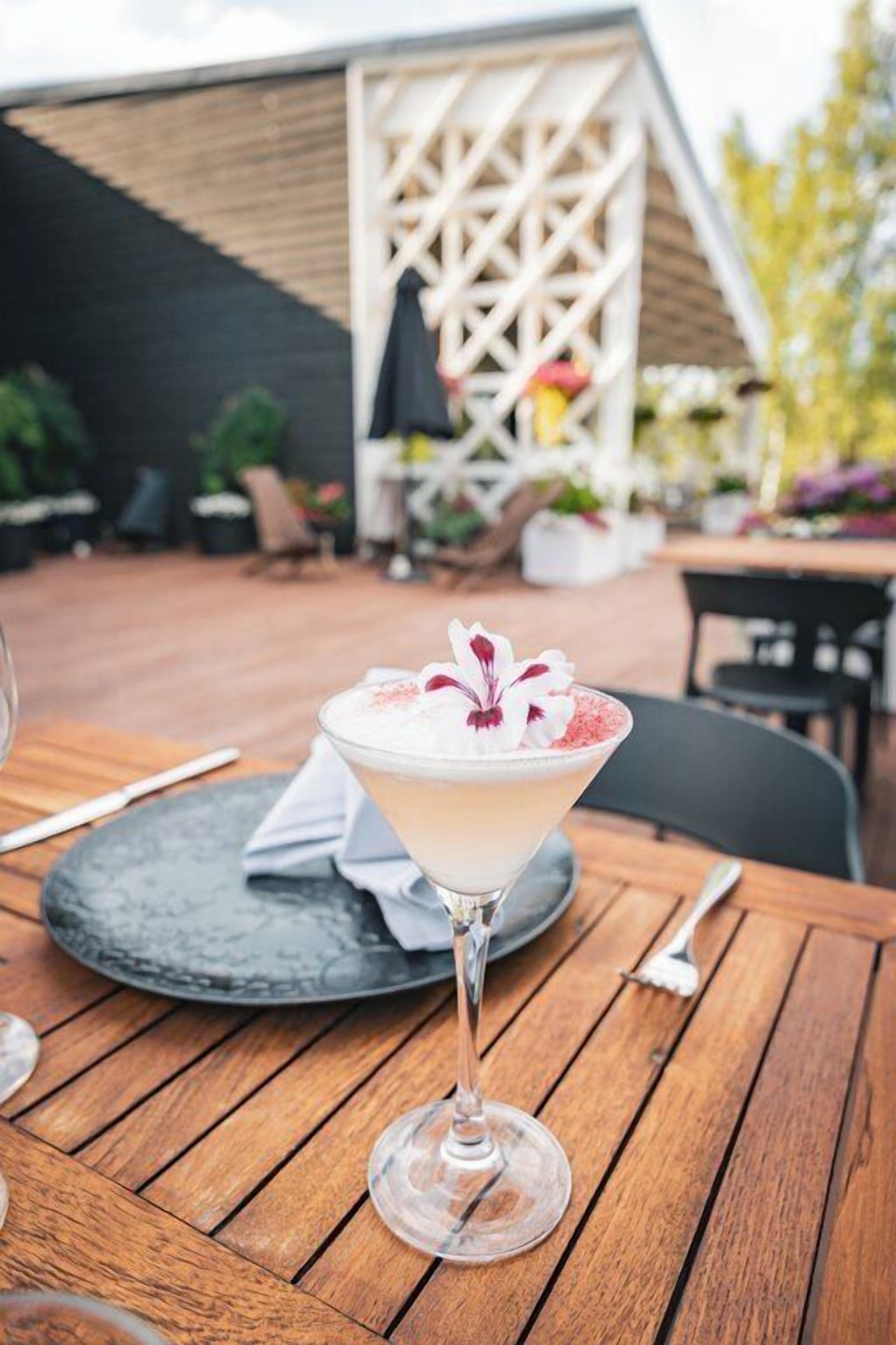A martini glass with a floral garnish on a wooden table outdoors.