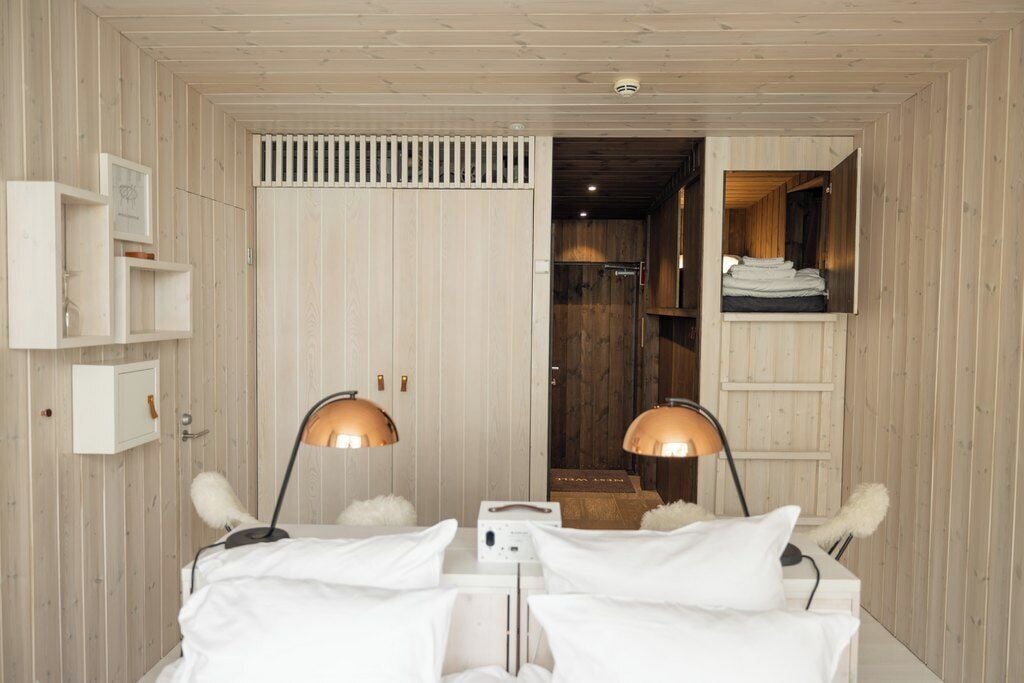 Quarto com duas camas, paredes de madeira, um guarda-roupa branco e um espelho.