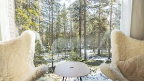 A room with two plush chairs facing a window overlooking a forested area with snow on the ground. - Arctic TreeHouse Hotel (Rovaniemi)