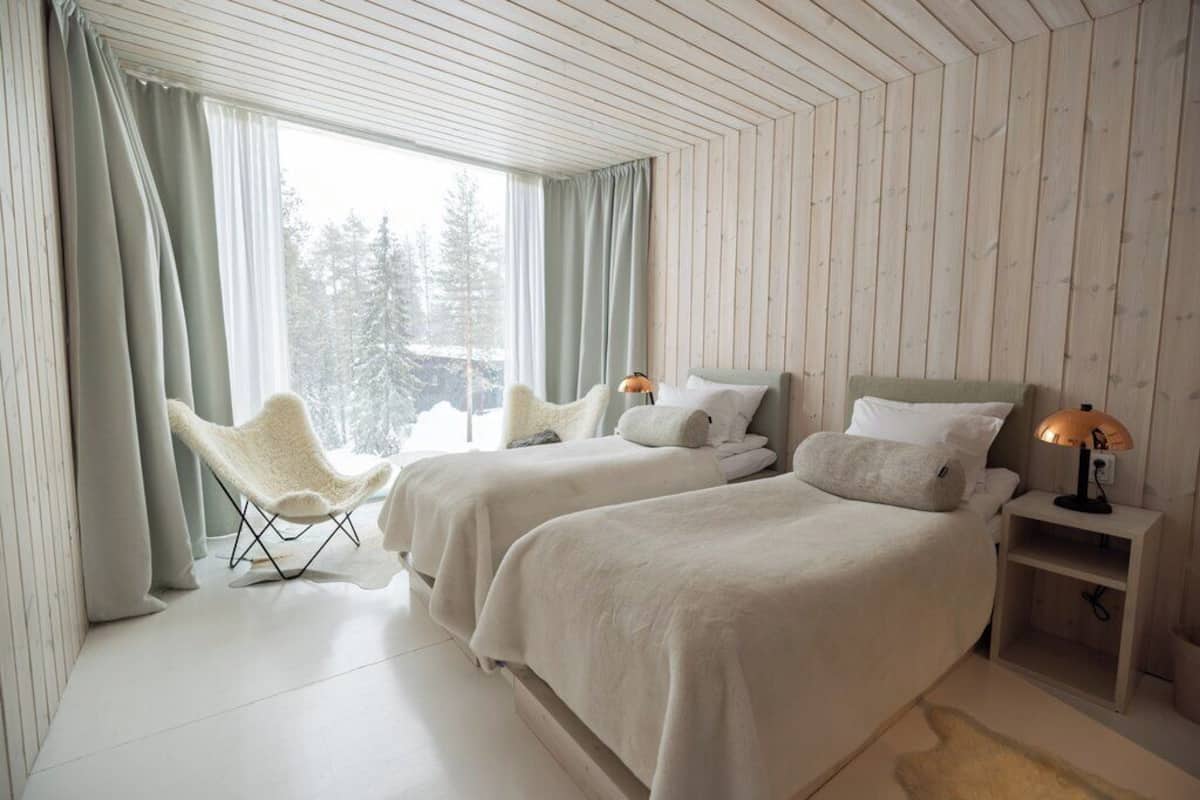 A bedroom with two beds, a chair, and a nightstand with a lamp.