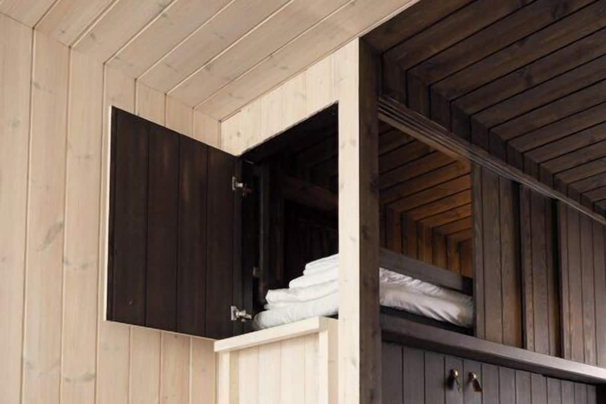A room with a wooden interior, a bed with a dark headboard, and a white storage unit with shelves.