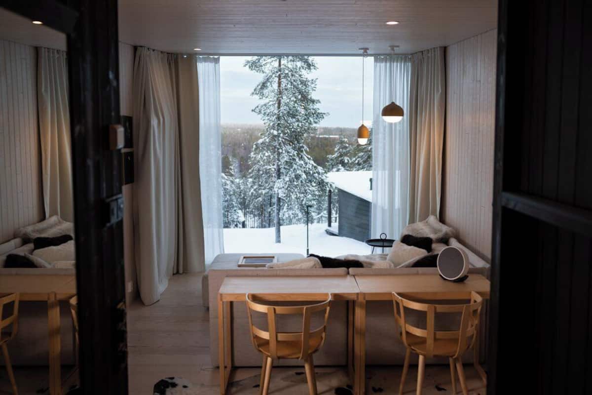 A modern room with a large window, wooden furniture, and a view of a snowy landscape.