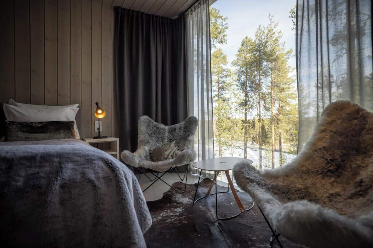 A room with a bed, a chair, a small table, and a window with a view of trees.
