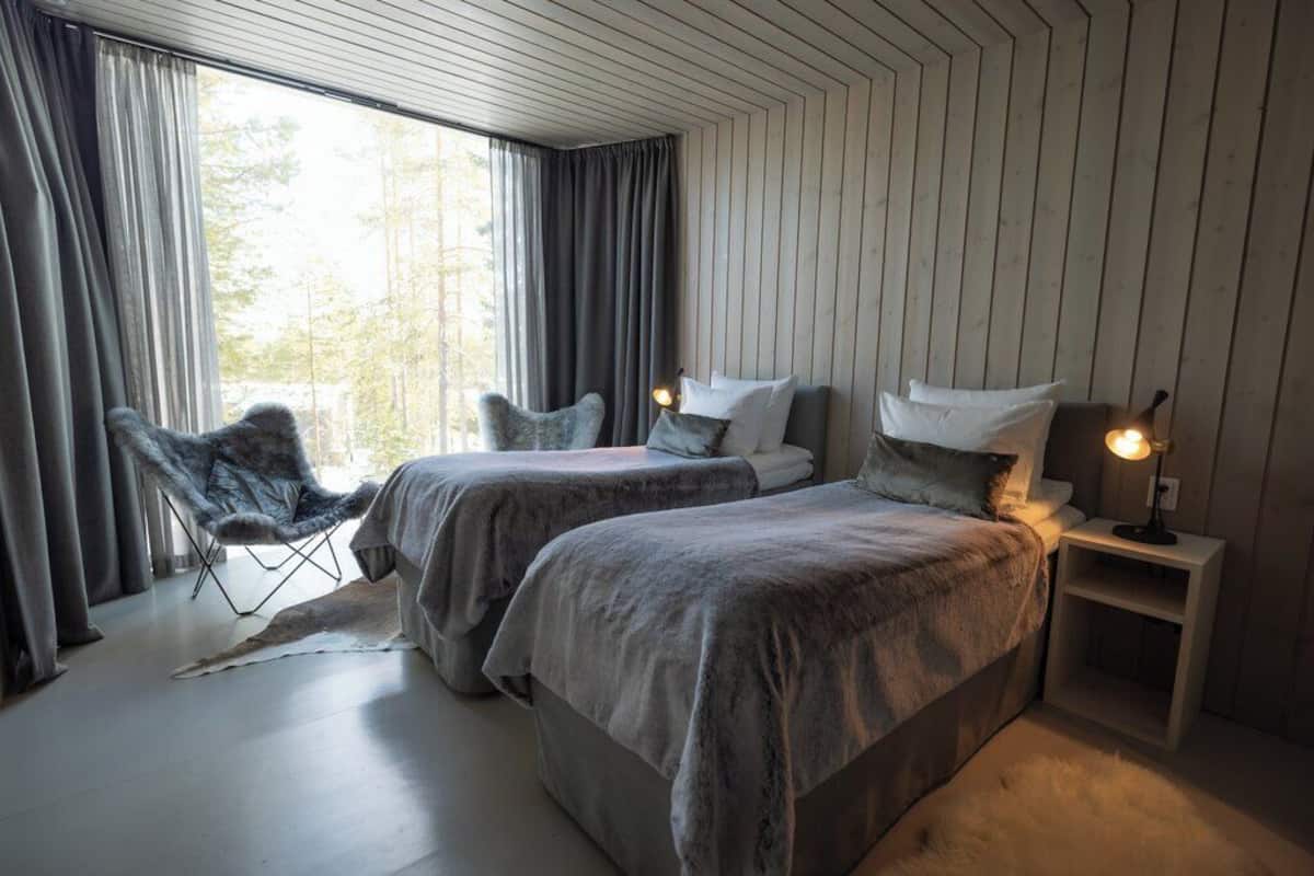 A bedroom with two beds, a chair, and a nightstand with a lamp.