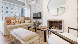 A modern living room with a sofa, ottoman, coffee table, fireplace, TV, and large mirror. - Genteel Home Retiro II (Madrid)