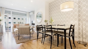 A modern dining area with a wooden table and chairs, a patterned wall, and a large window offering a view of buildings. - Genteel Home Retiro II (Madrid)