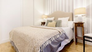 A neatly arranged bedroom with a large bed, two bedside tables with lamps, and a striped wall. - Genteel Home Retiro II (Madrid)