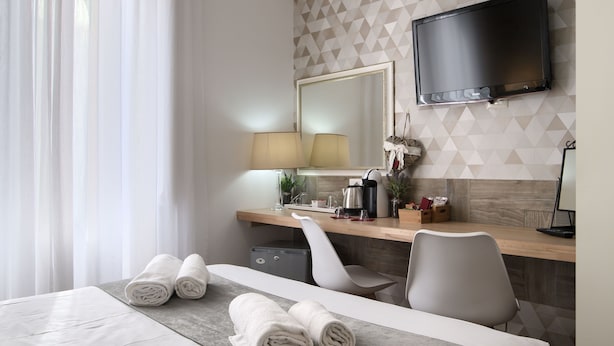 A hotel room with a bed, a desk, a chair, a TV, and a mirror. - Domus Pietro Inn (Rome)