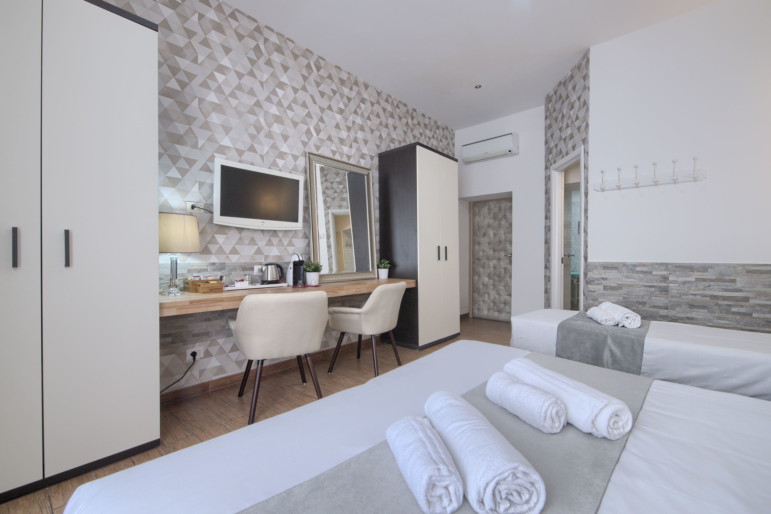 Une chambre d’hôtel équipée d’un bureau, de deux lits, d’une télévision et d’un miroir.