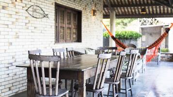 A covered outdoor dining area with a brick wall, wooden chairs, and a table.