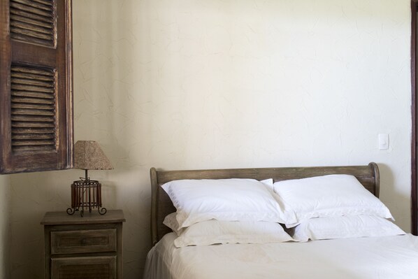 A bed with white linens and a wooden headboard, a nightstand with a lamp, and a wall with a textured pattern. - Villa do Vento (Fortim)