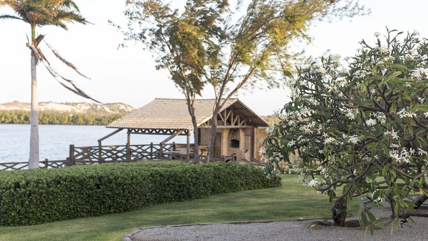 A lakeside lodge with a wooden deck, a thatched roof structure, and a well-maintained lawn.