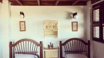 A room with two wooden beds, a small wooden nightstand, a cabinet, and a window with shutters.