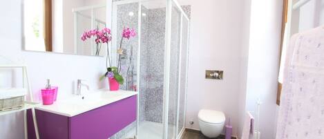 Un baño con cabina de ducha, inodoro y lavabo con tocador morado.