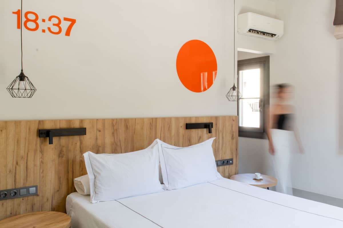 Ett modernt hotellrum med en sänggavel i trä, vita sängkläder och en stor, orange väggdekoration.