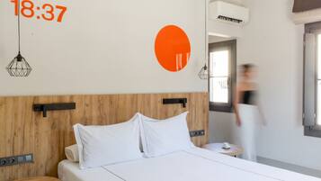 Een moderne hotelkamer met een houten hoofdbord, witte beddengoed en een grote oranje wanddecoratie.