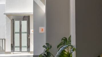A modern building interior with a glass elevator, potted plants, and a number sign indicating the location.