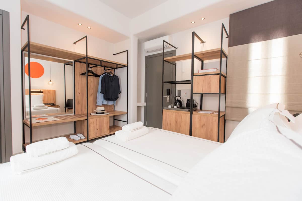 Ett modernt hotellrum med en säng, en garderob i trä, ett skrivbord med en stol och en klädstång med kläder.
