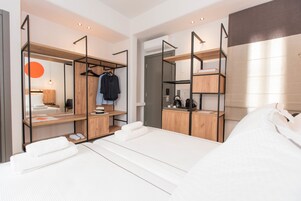 Una camera d'albergo moderna con un letto, un armadio in legno, una scrivania con una sedia e un appendiabiti con vestiti.
