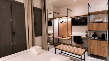 A modern hotel room with a large bed, a desk, a chair, a wardrobe, and a TV.