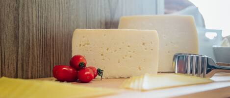 A wooden cutting board with a wedge of cheese, a cheese knife, and a few cherry tomatoes.