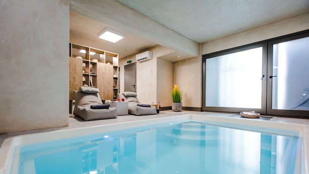 Un espace spa comprenant une grande piscine intérieure, des sièges et une fenêtre en verre dépoli.