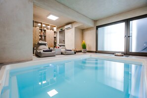 A spa area with a large indoor pool, seating, and a window with frosted glass. - Sandom (Paros)