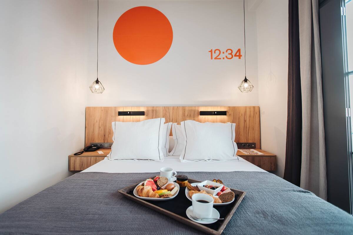 Ett hotellrum med en säng, ett brickbord med frukost och en väggklocka som visar 12:34.