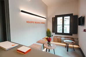 A modern reception area with a welcoming sign, a seating area with a vase of flowers, and a flat-screen TV mounted on the wall.