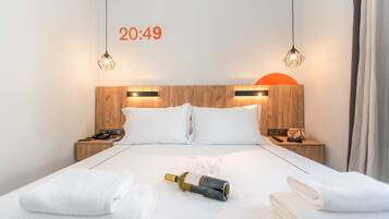 Une chambre d’hôtel avec une tête de lit en bois, deux lampes de chevet, un lit avec du linge de lit blanc, une bouteille de vin et une horloge indiquant 20 h 49.