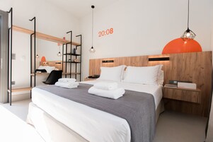 Una habitación de hotel moderna con una cama grande, cabecera de madera y una mesita de noche con lámpara.