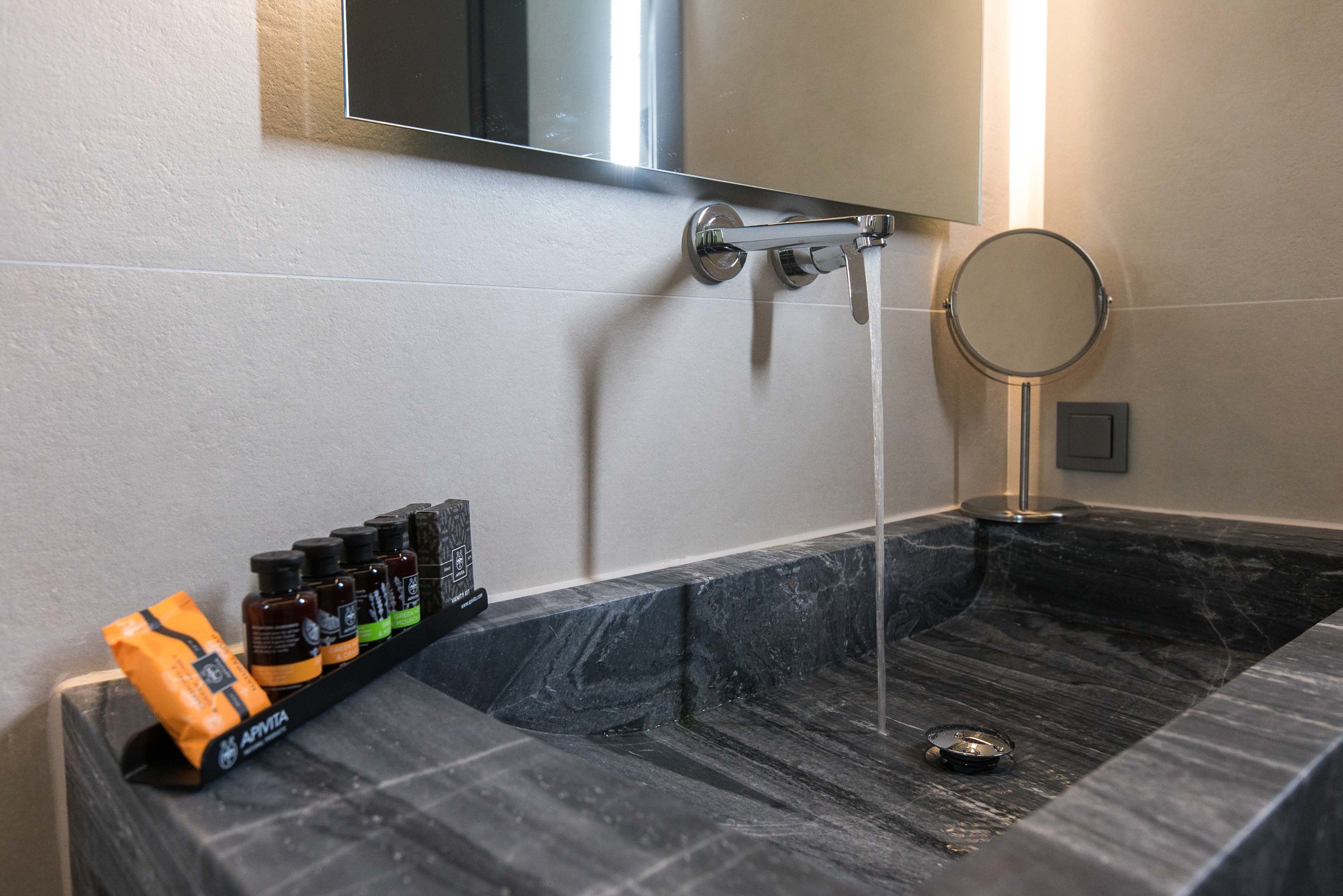Un baño con lavamanos de mármol, un espejo y un estante con artículos de aseo.