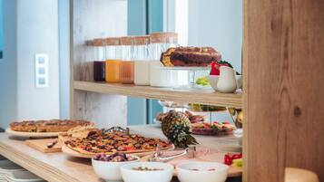 A buffet table with various food items including a pineapple, bowls of fruits, and a variety of desserts.