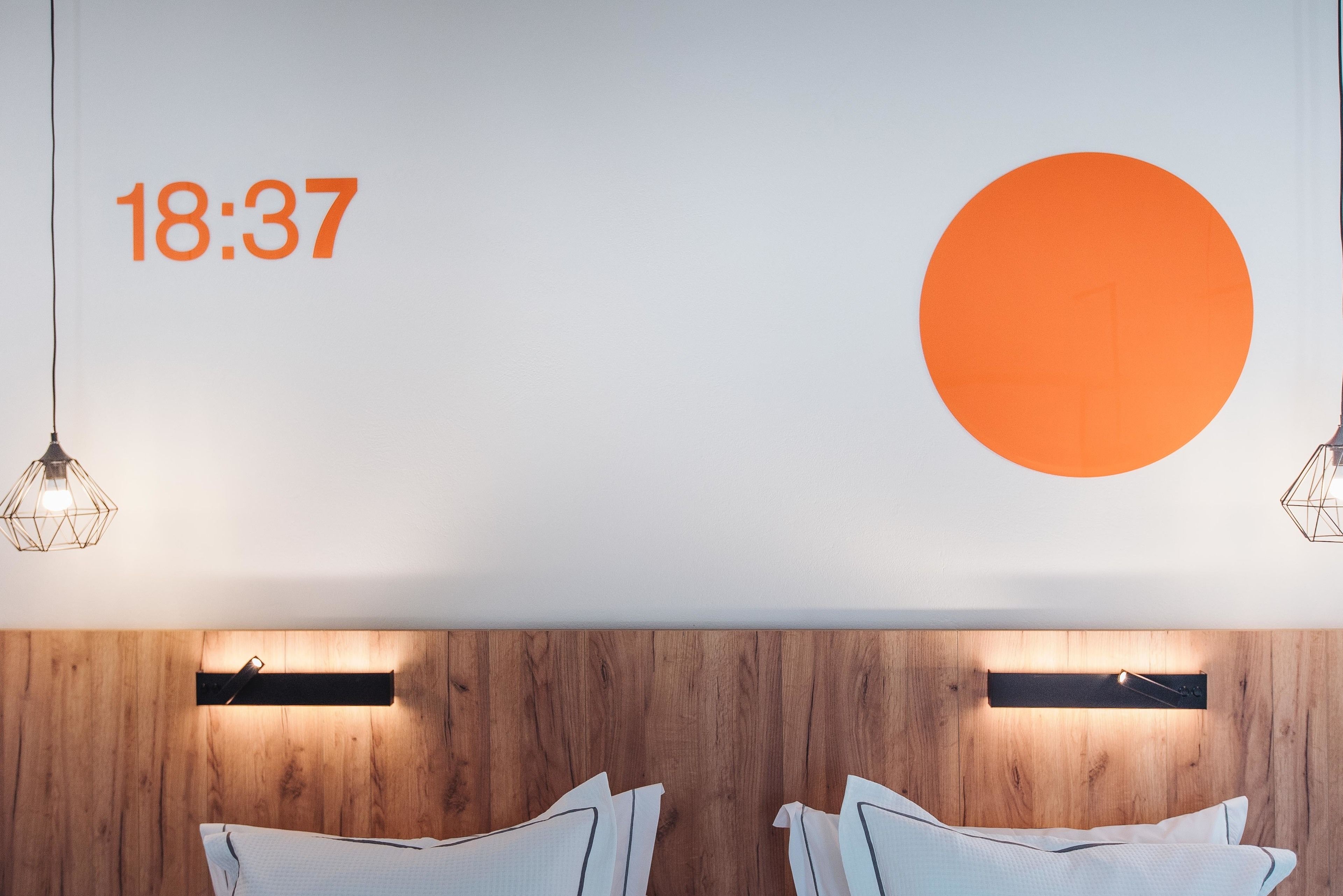 Habitación de hotel moderna con cabecera de madera, dos mesitas de noche y un gran círculo naranja en la pared.